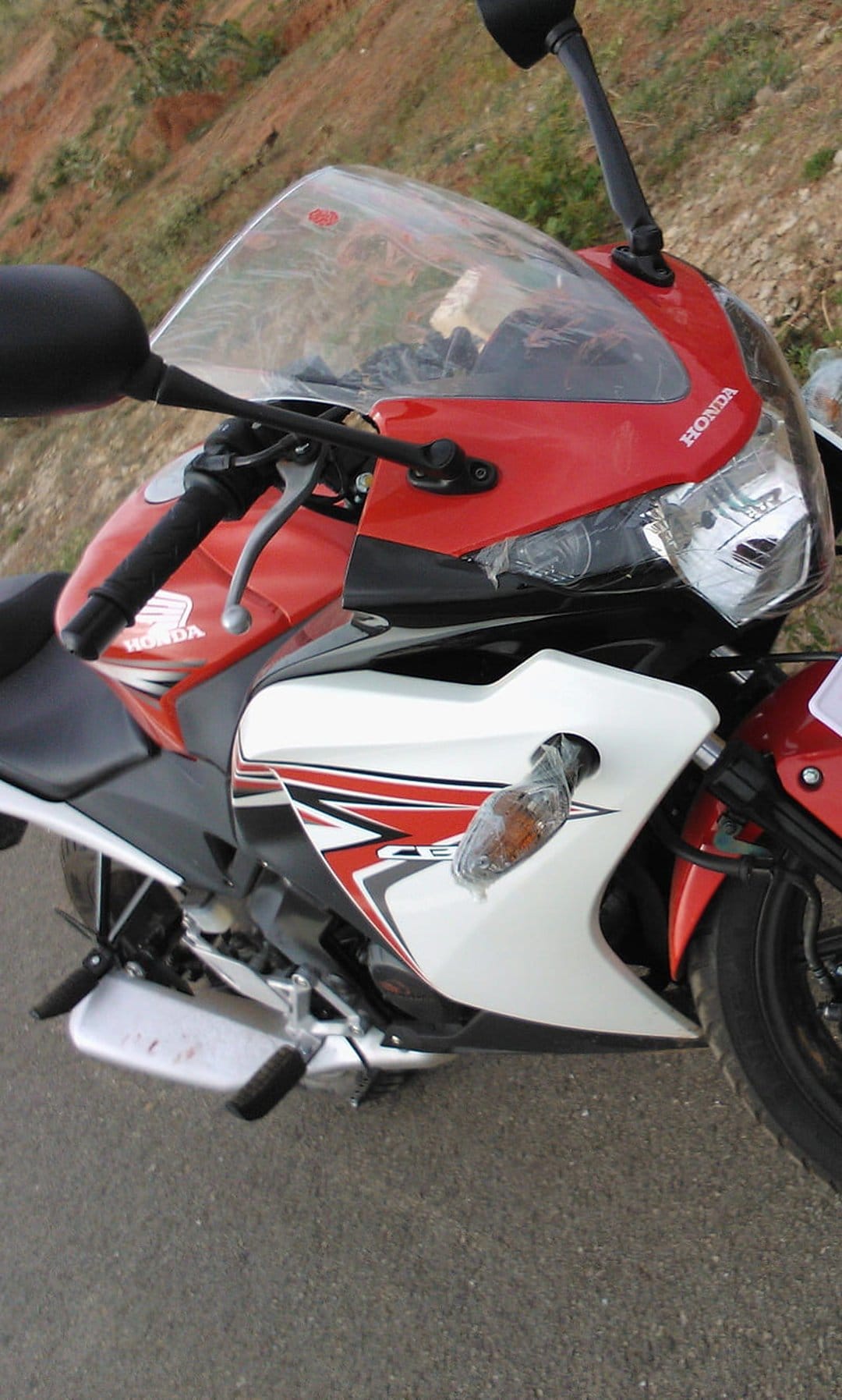 Honda CBR motorcycle with red fairing graphics and clear windshield parked on asphalt against blurred hills.
