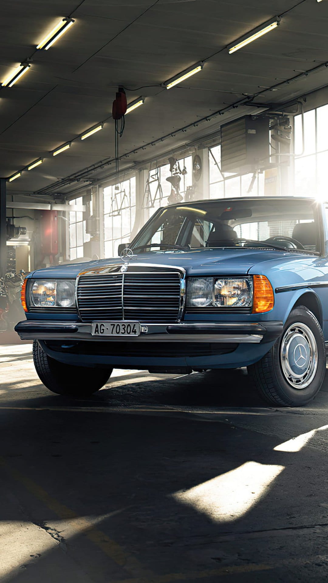 Mercedes-Benz W123 sedan in a vintage garage illuminated by warm fluorescent lights showing the chrome grille.