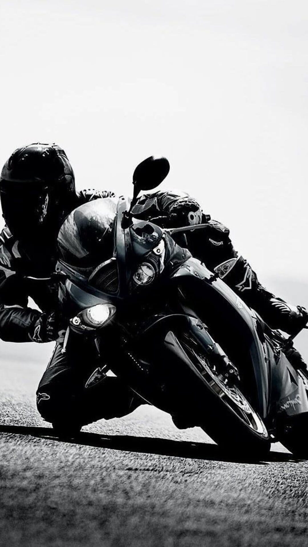 Professional motorcyclist in a dark racing suit leans into a sharp turn on a track with glowing headlights.