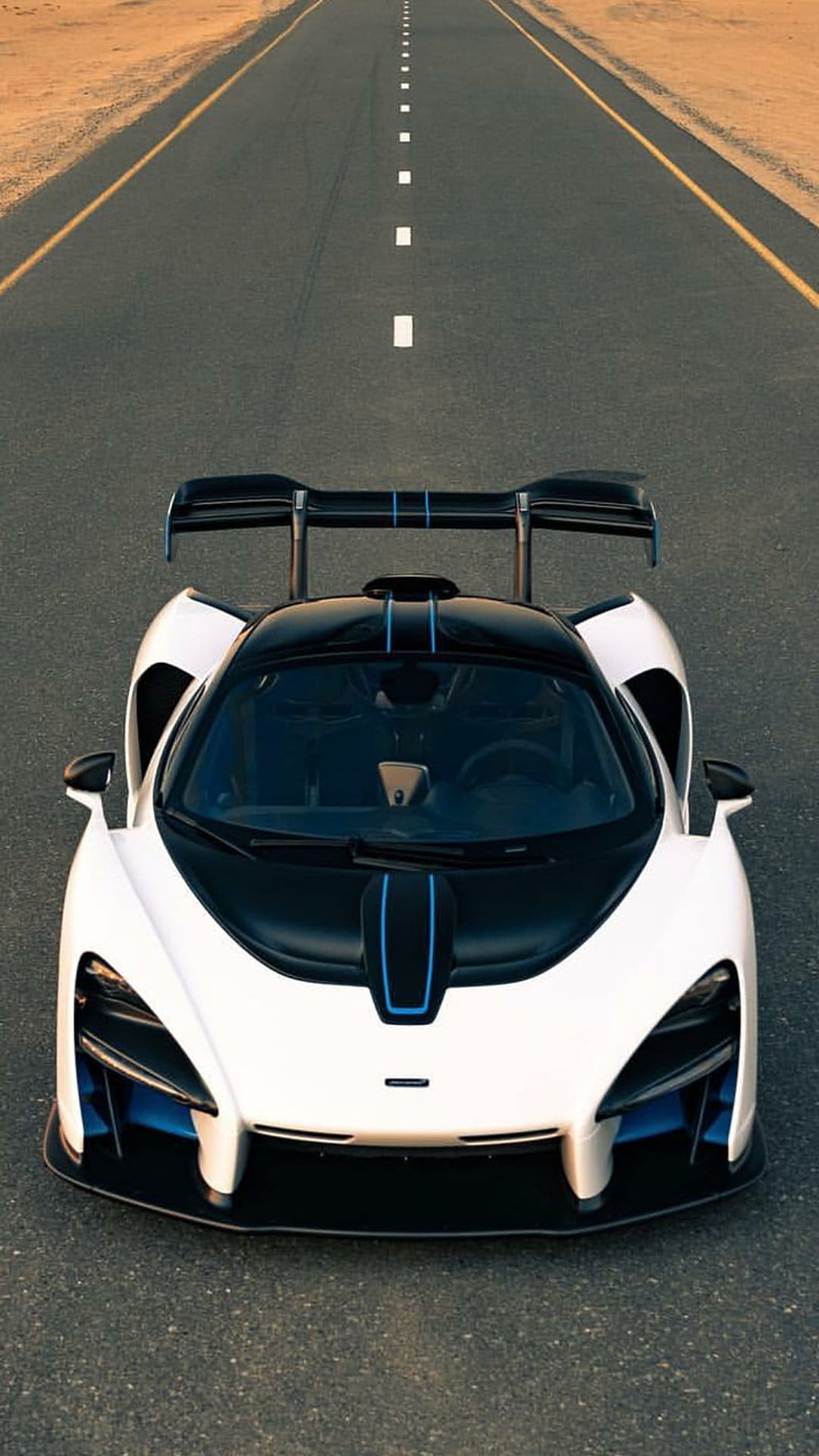 McLaren Senna supercar with blue accents drives along a desert highway from an overhead aerial perspective.