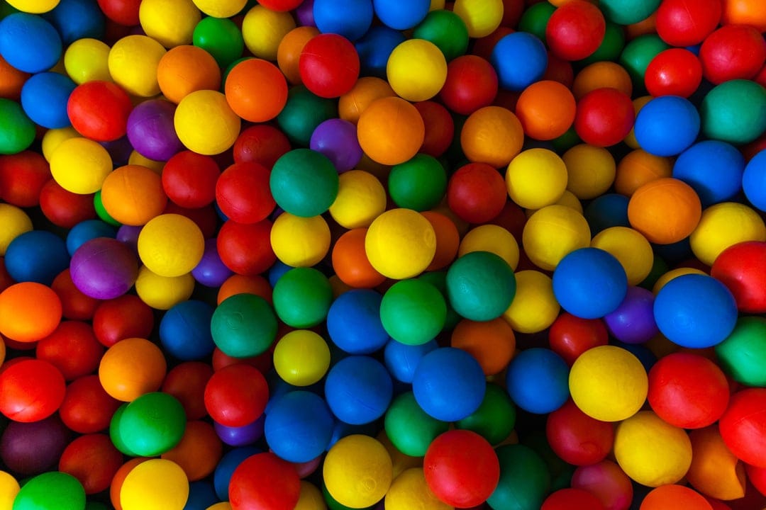 Red, blue, and yellow plastic spheres packed tightly in an overhead view, creating a textured rainbow pattern.