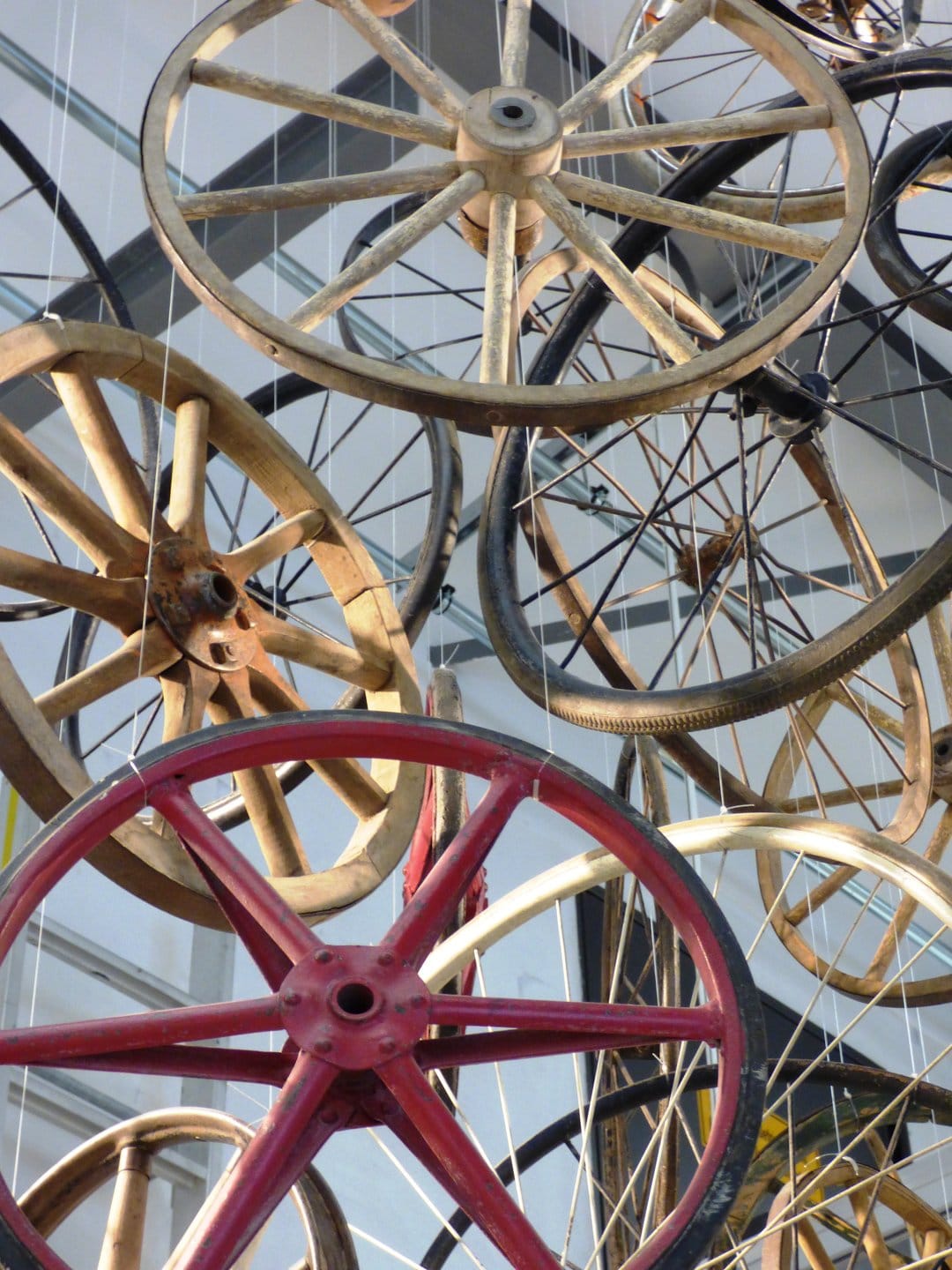 Vintage wooden and iron wheels hang in a bright gallery space, showcasing circular spokes and weathered textures.