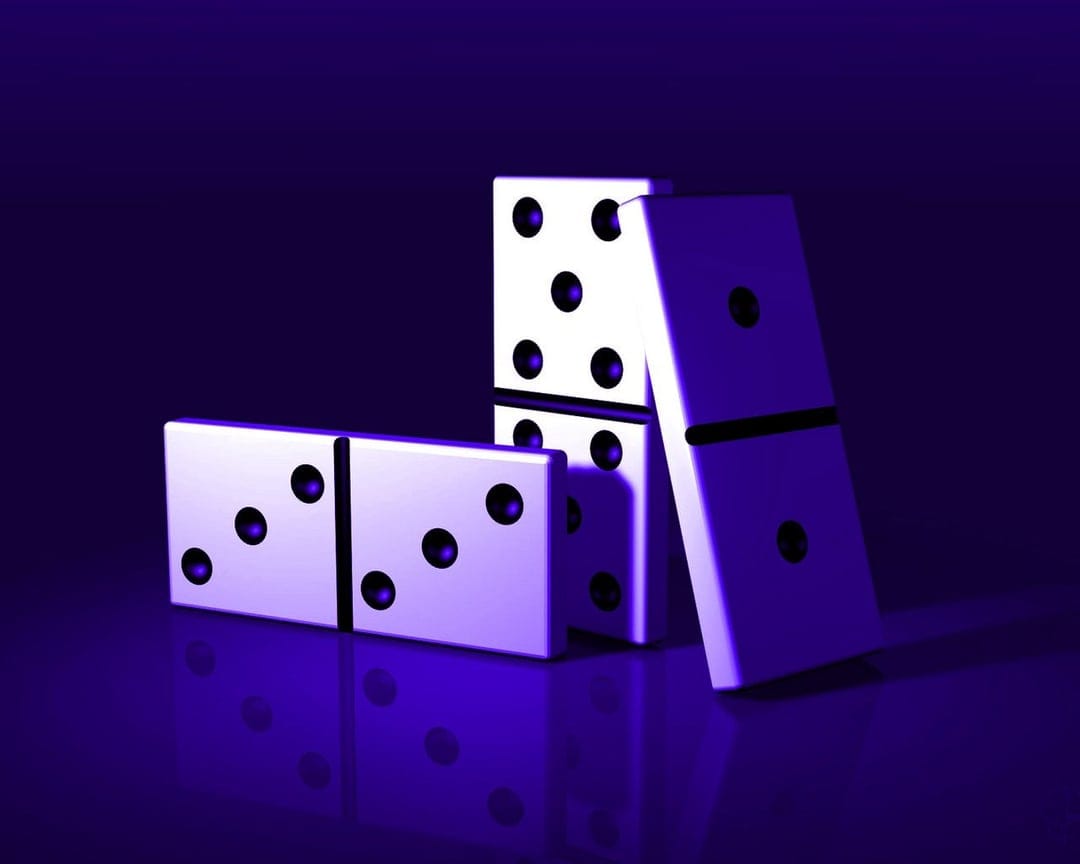 White dominoes with black pips lean against each other under a vivid purple light on a dark reflective surface.
