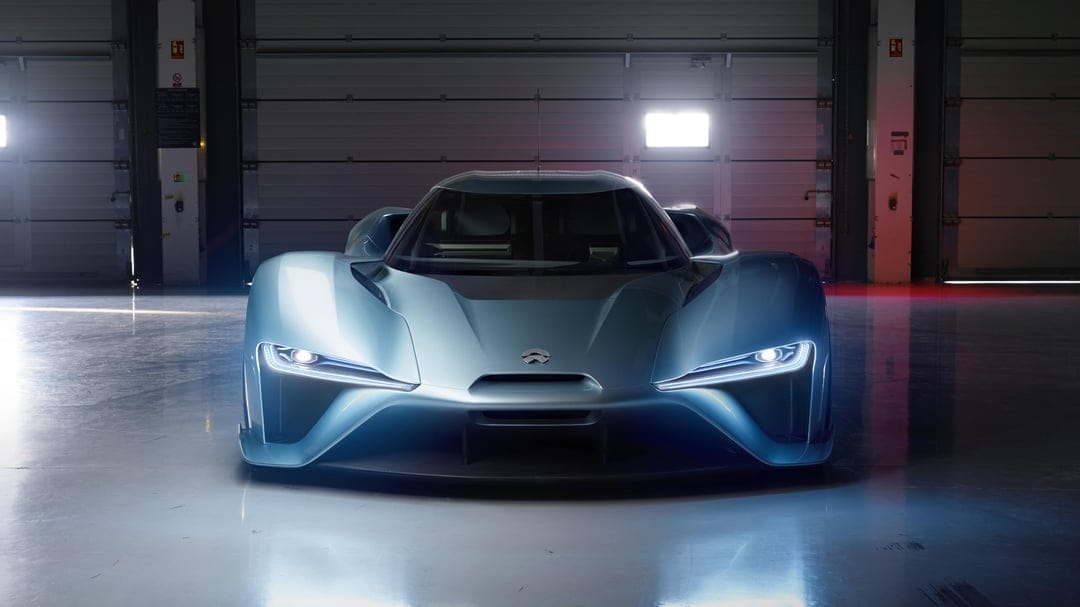 Light blue Nio EP9 electric supercar with glowing LED headlights parked in a dark industrial studio garage.