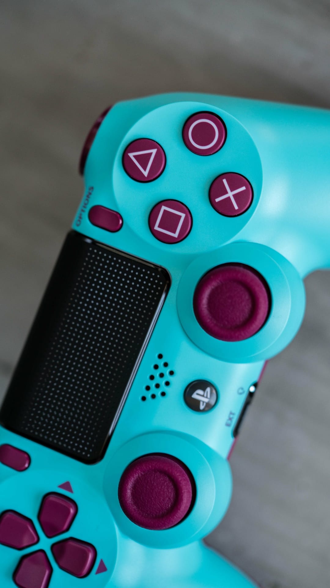 Turquoise PlayStation 4 controller with purple action buttons and black analog sticks in a close-up shot.