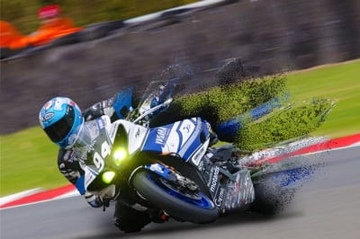 Motorcyclist in blue racing gear leans a Yamaha bike low into a sharp curve on a blurred asphalt track.