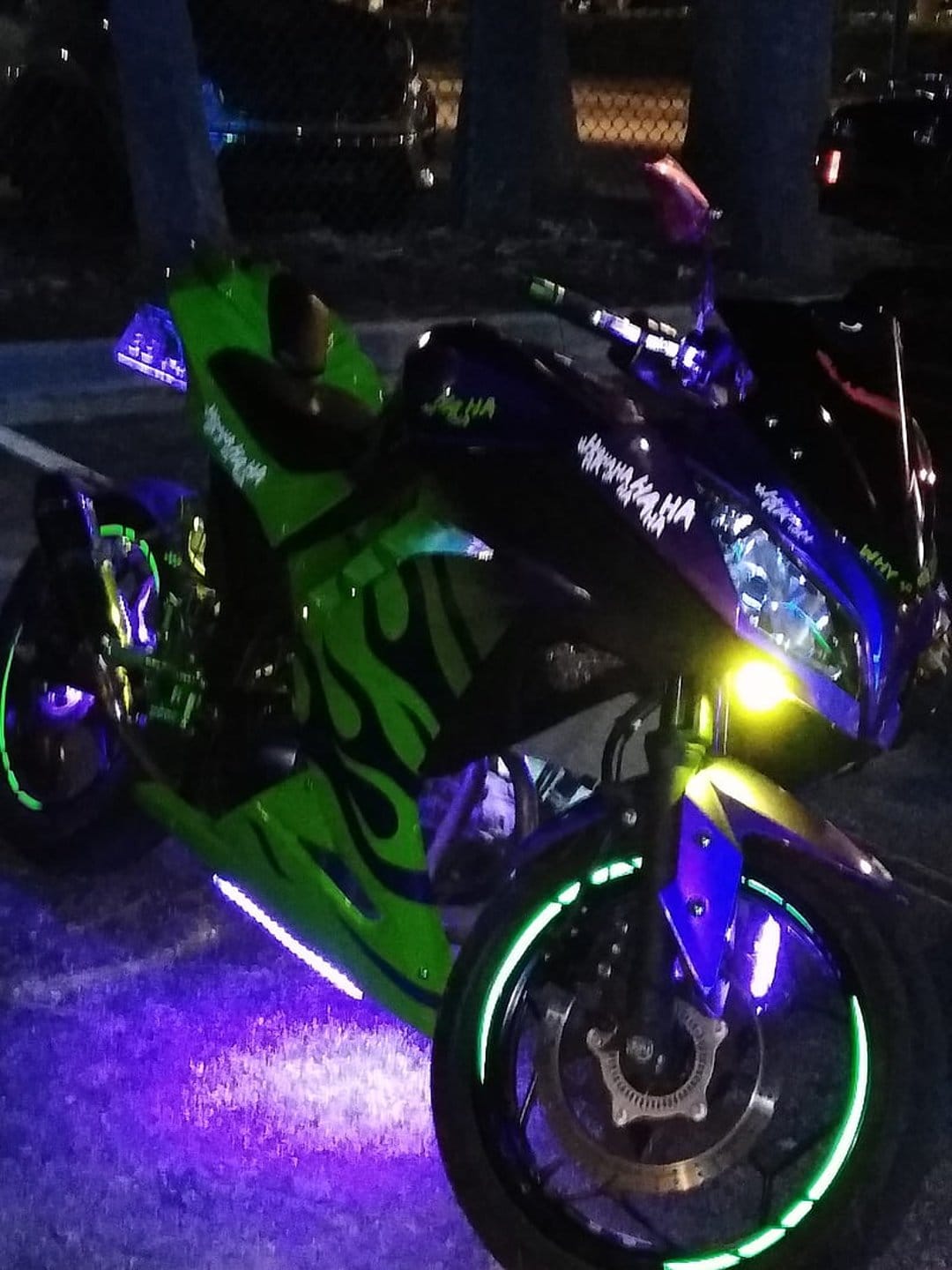 Custom sportbike featuring neon green flame decals and blue LED underglow glows against a dark night backdrop.