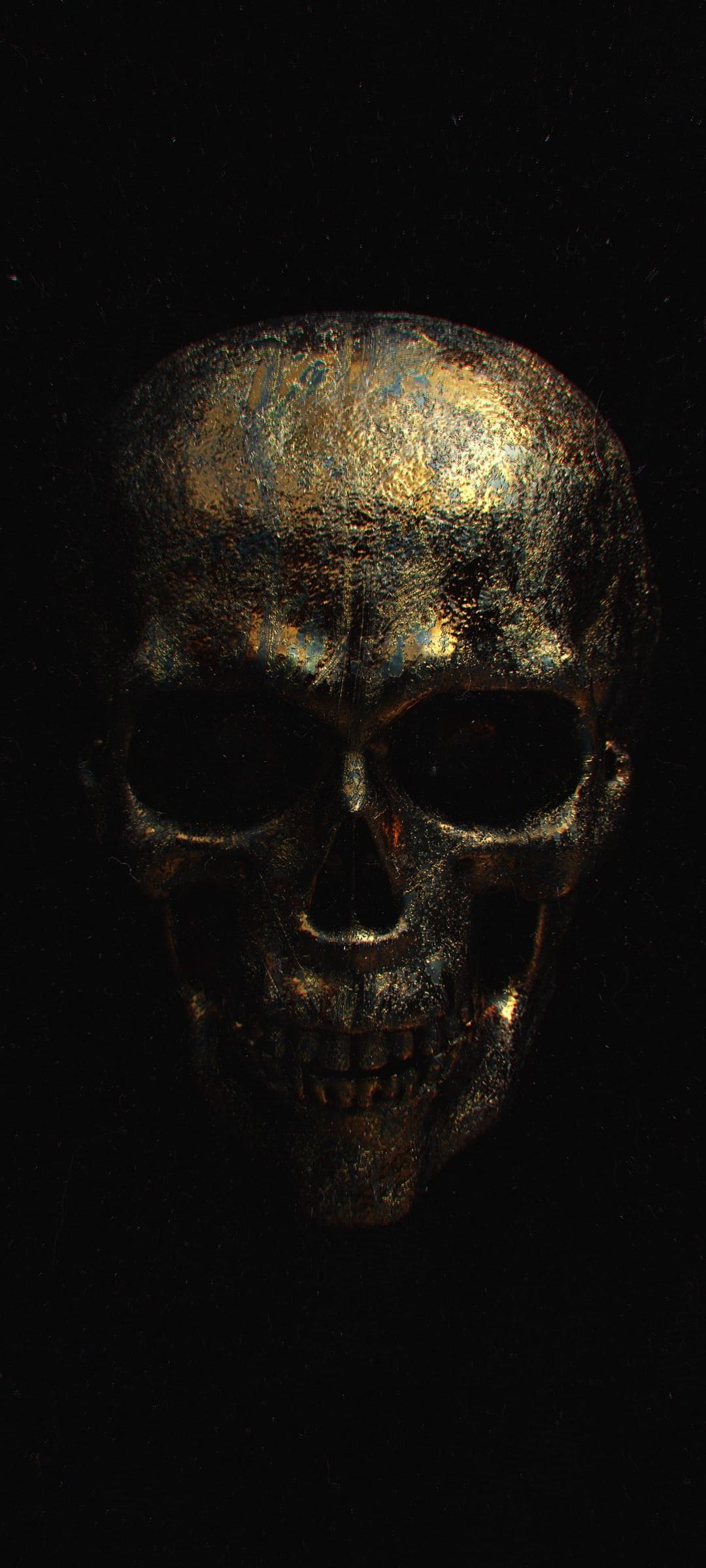 Golden skull with a distressed metallic texture and deep black eye sockets illuminated by soft directional light.