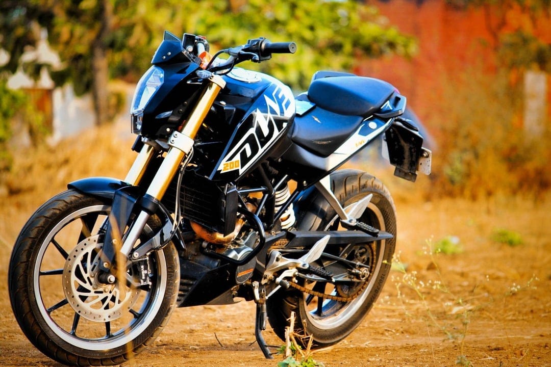 Black KTM Duke 200 motorcycle with gold forks and blue seat parked on a dry dirt path during golden hour.