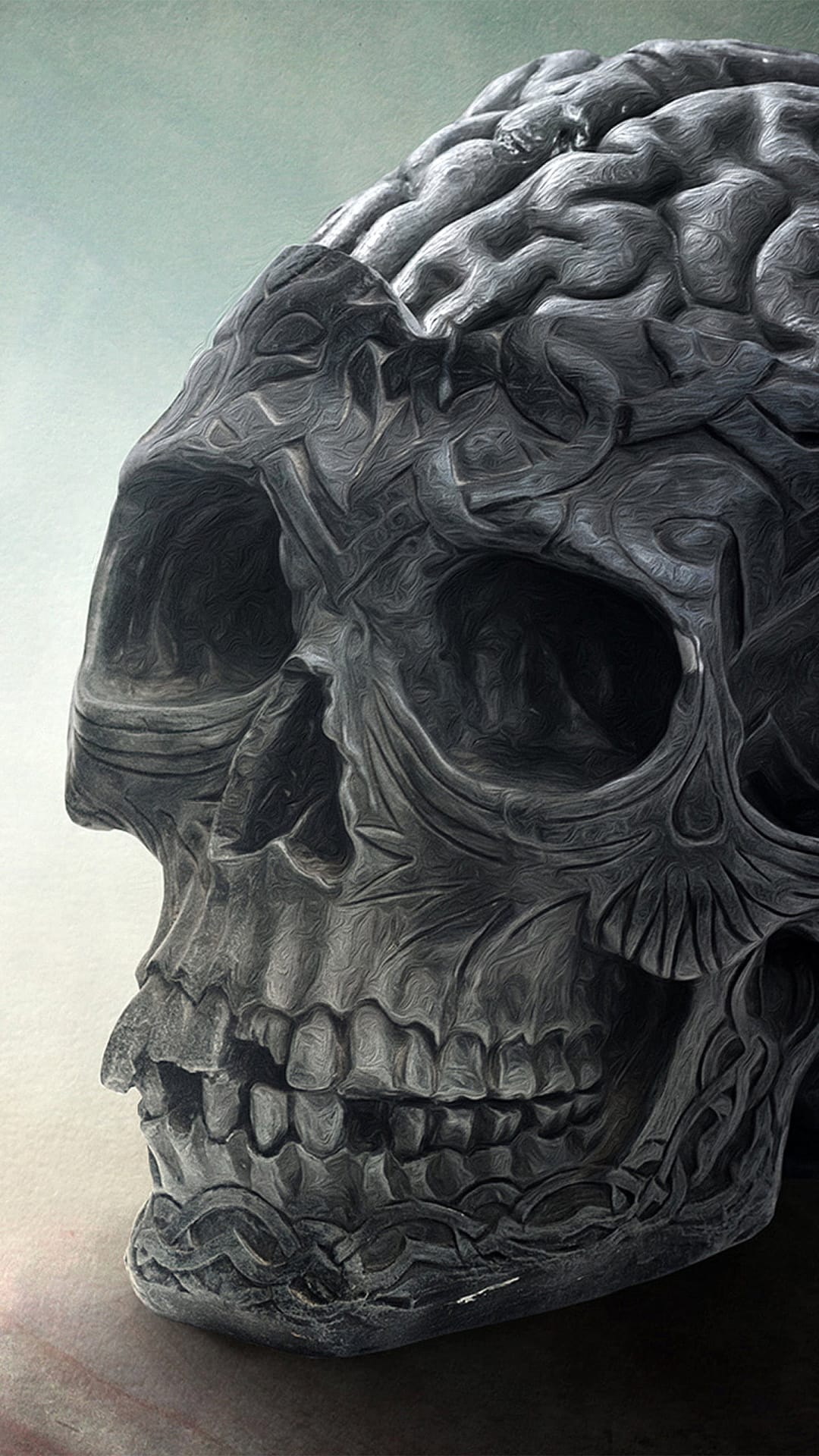 Stone skull with a brain-like cranium texture featuring deep shadowed eye sockets and weathered grey surfaces.
