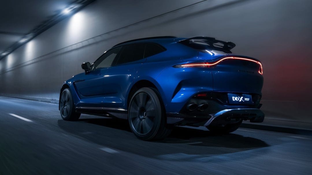 Blue Aston Martin DBX 707 driving through a dark tunnel with red glowing taillights and motion blur.