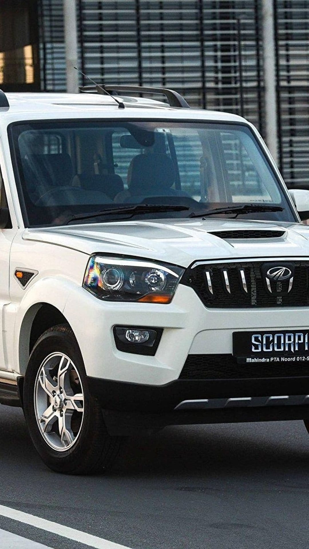 White Mahindra Scorpio SUV showing a chrome grille and headlights against a modern glass building background.