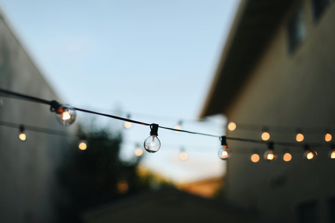 Clear round light bulbs on a wire glow softly against a deep blue twilight sky with blurred building silhouettes.