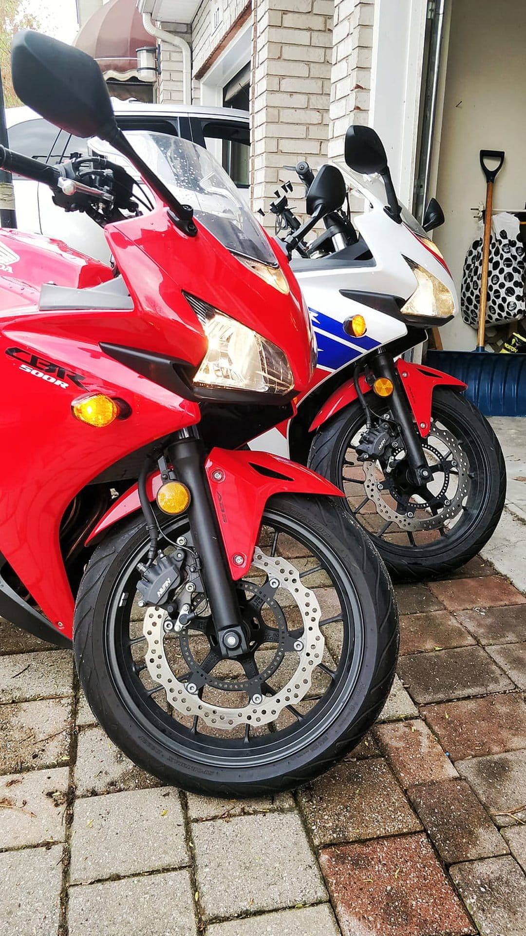 Red and white sport motorcycles parked in a driveway, showing disc brakes, fairings, and racing stripes.