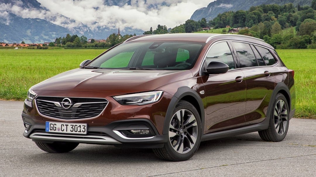 Brown Opel Insignia Country Tourer wagon on a road with green fields and misty mountains in the background.
