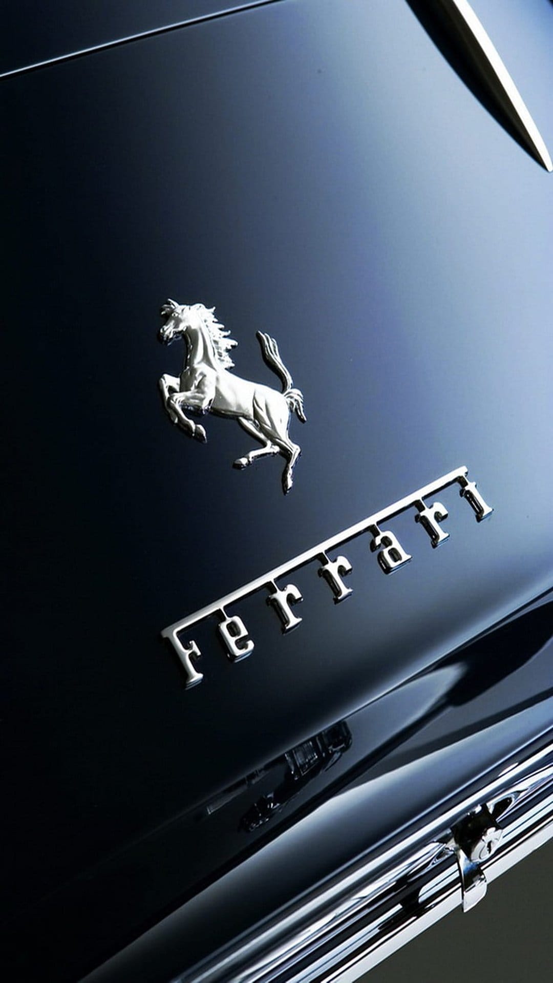 Silver Ferrari prancing horse emblem and logo script on a polished dark blue metallic car hood with reflections.