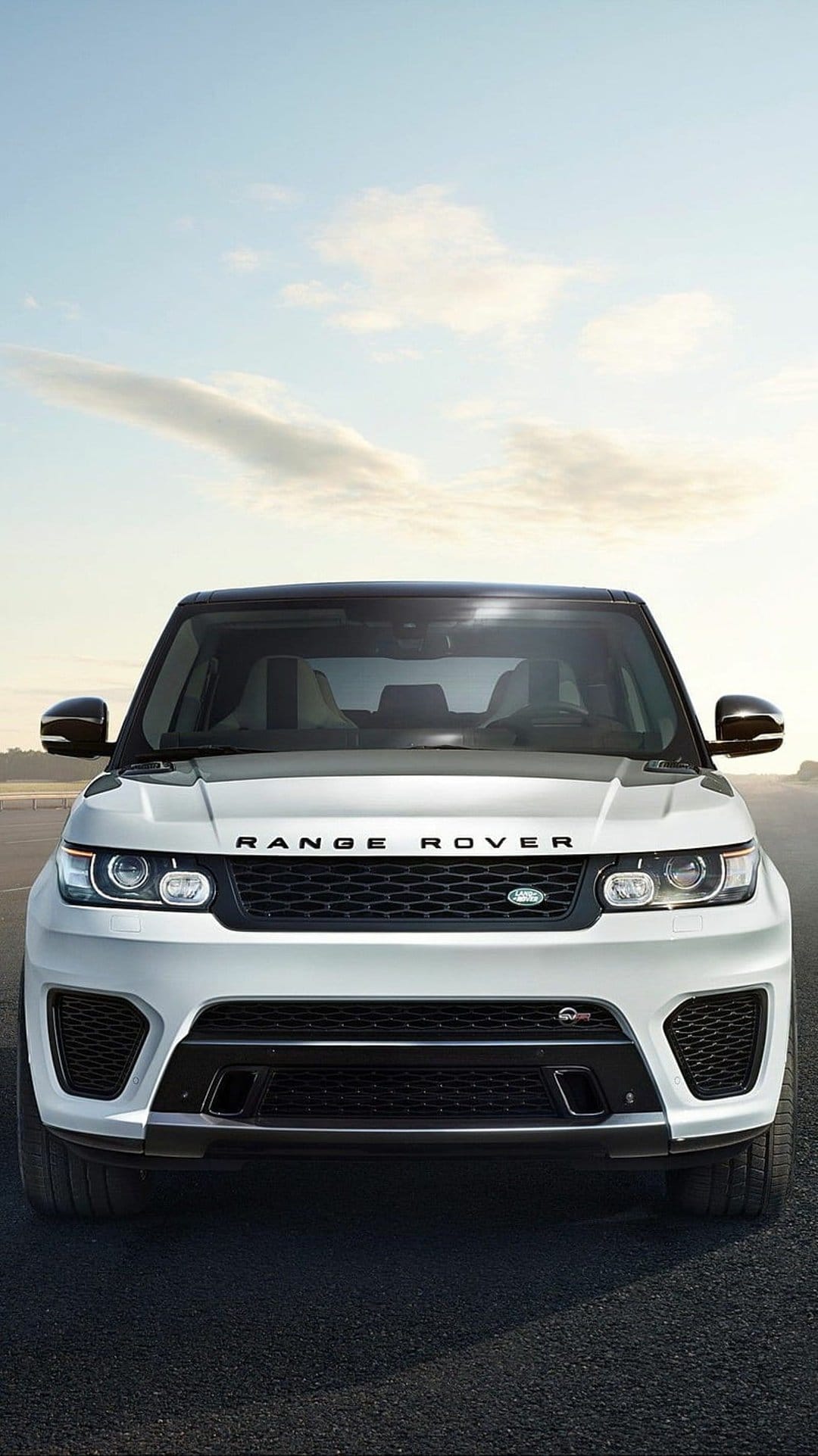 White Range Rover Sport SUV parked on a dark asphalt road under a clear blue sky with light clouds in front view.