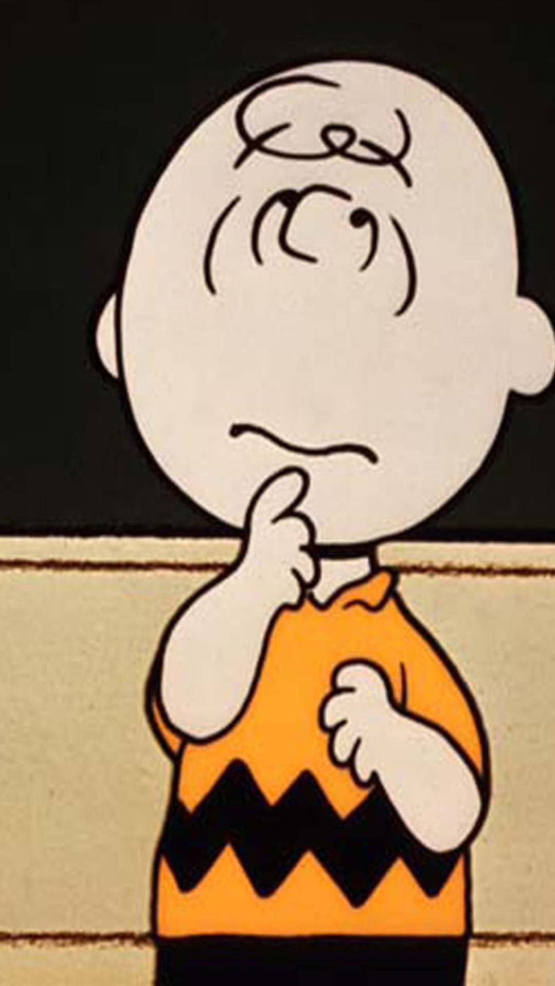 Charlie Brown rests a hand on his chin with a thoughtful expression while wearing his signature zig-zag polo shirt.