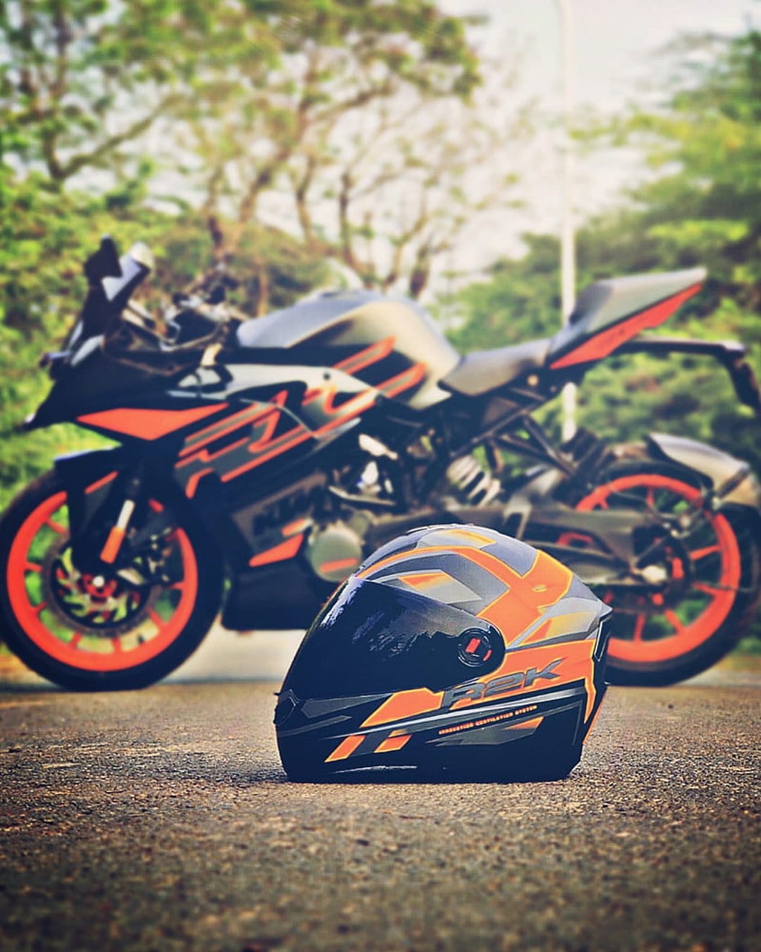 KTM sports bike with orange accents parked behind a matching full-face helmet on a gray asphalt road surface.