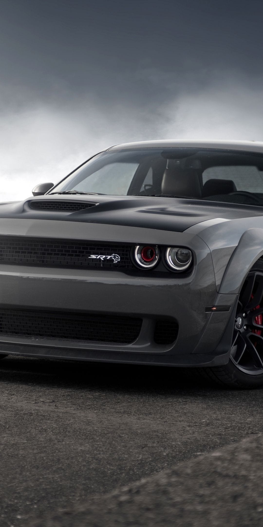 Dodge Challenger SRT Hellcat with widebody fenders and red air intake headlights against a cloudy sky.