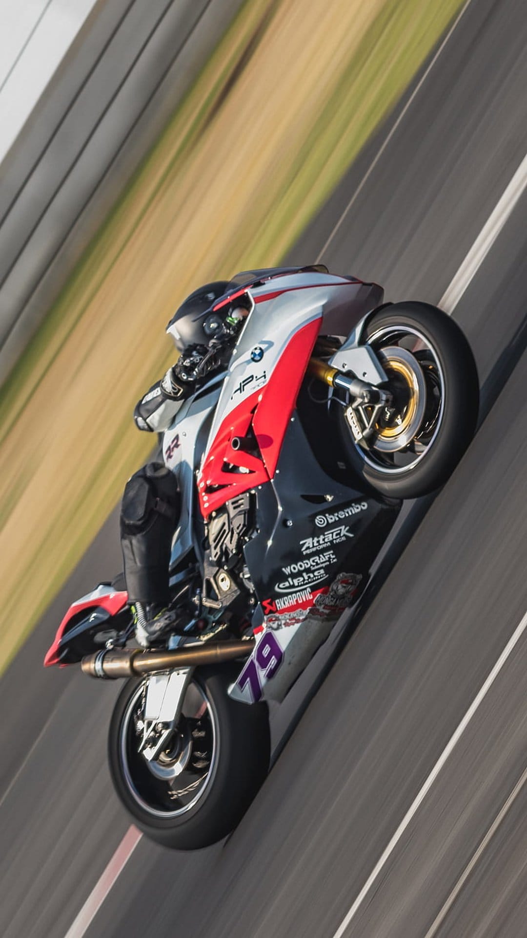 Motorcyclist in racing gear performs a wheelie on a BMW HP4 superbike with visible Brembo decals on a track.