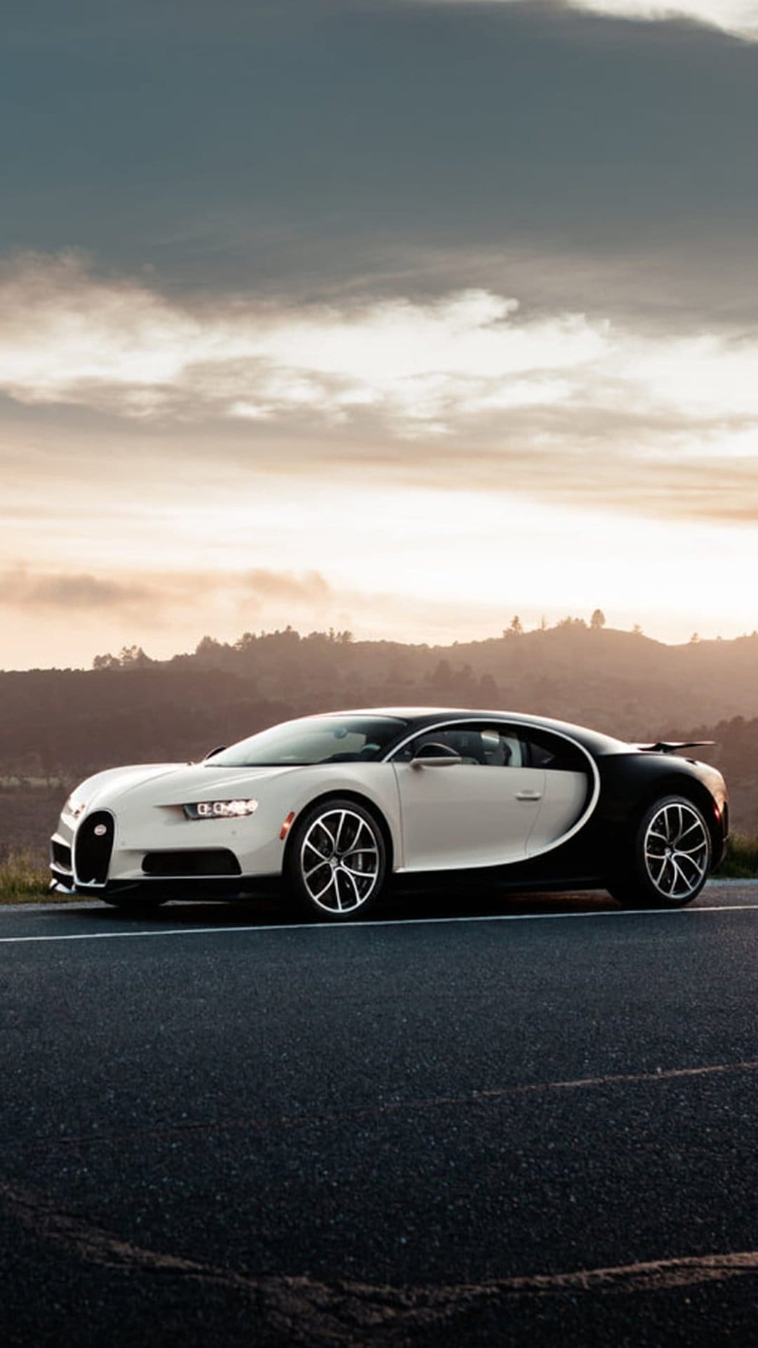 Bugatti Chiron supercar in white and black parked on a rural road during a golden sunset with distant green hills.