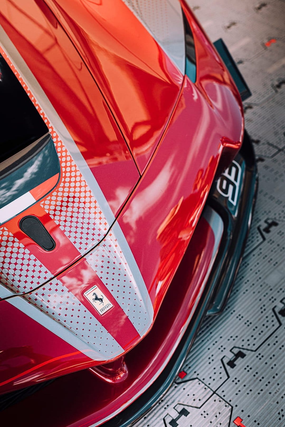 Ferrari racing car hood with a silver logo, red paint, white racing stripes, and a high-tech floor texture.