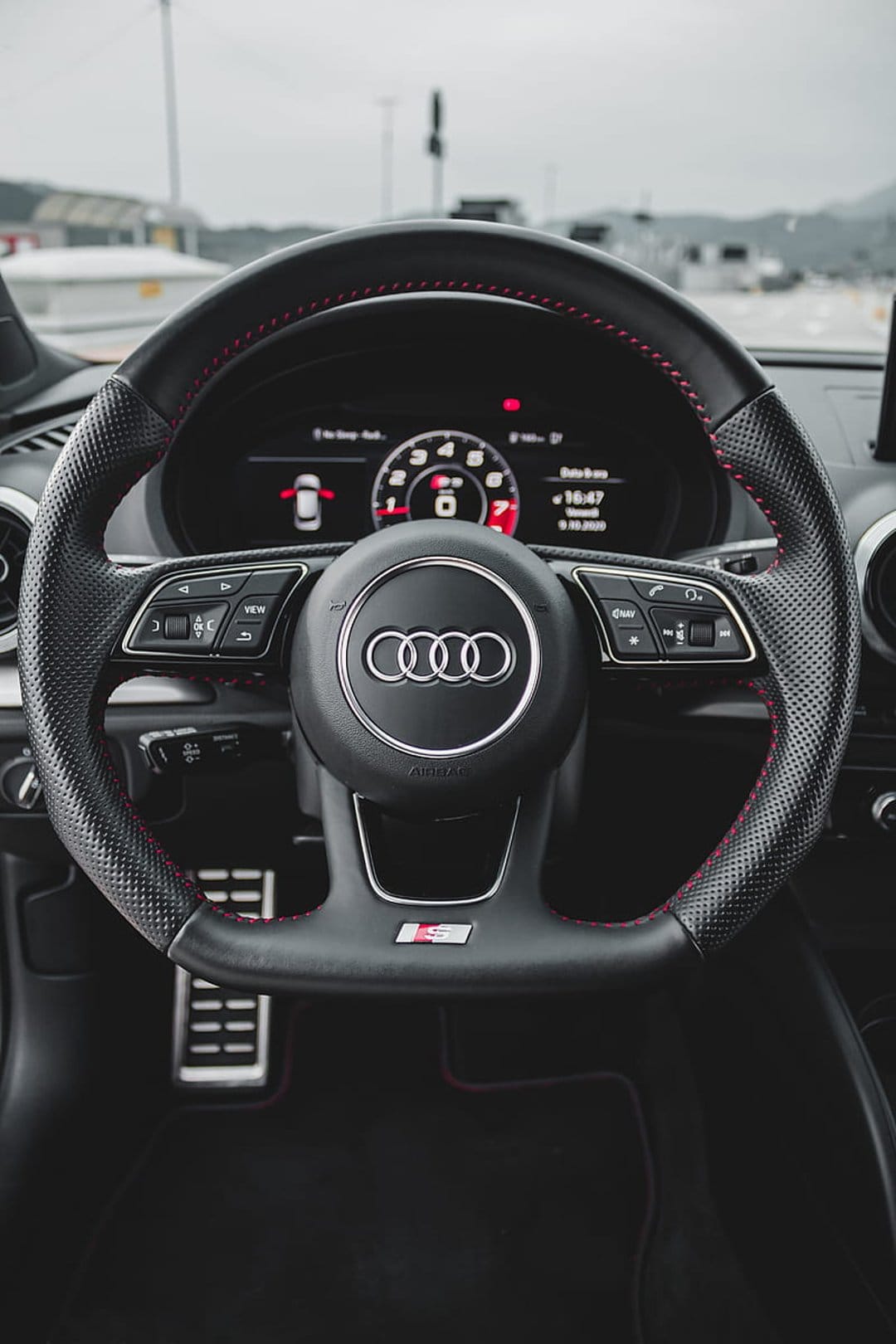 Audi RS steering wheel featuring red stitching and a digital dashboard inside a modern luxury vehicle cockpit.