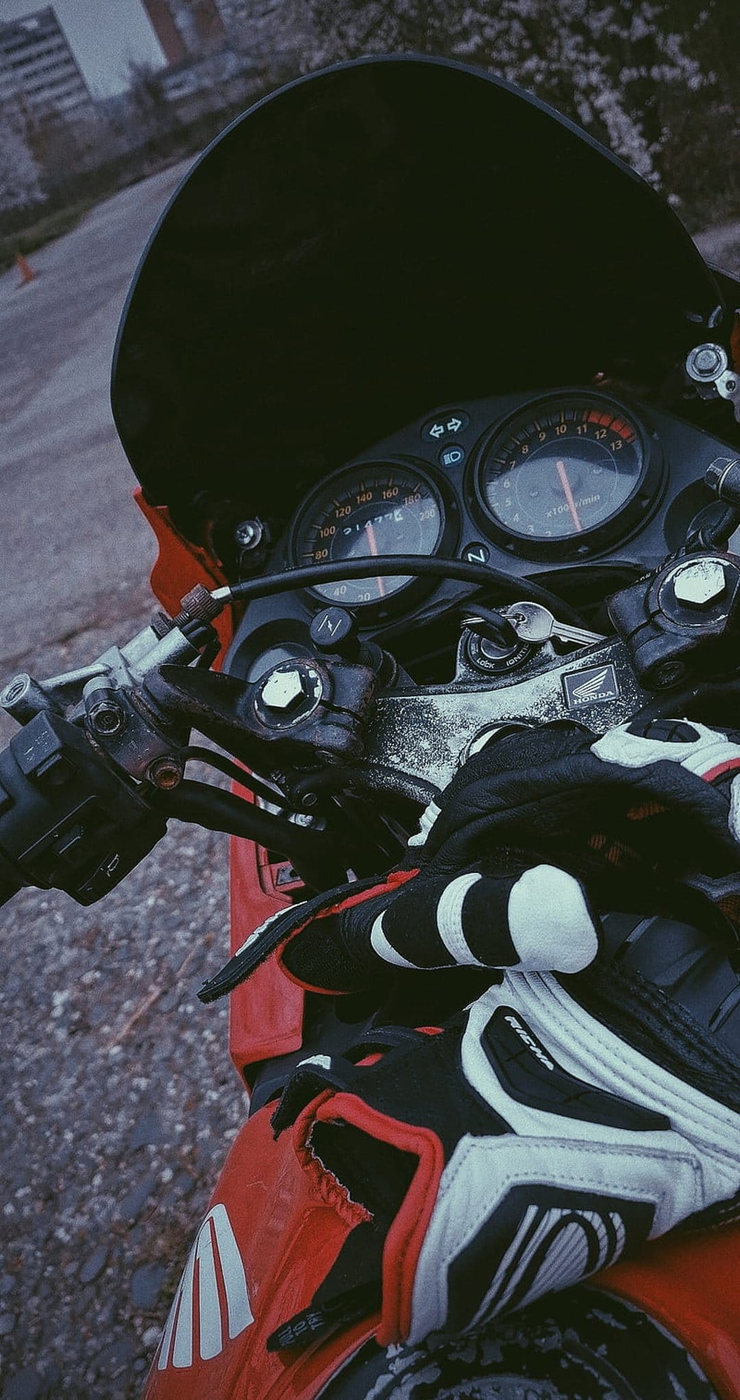 Racing gloves and dual motorcycle gauges sit atop a red sportbike cockpit with an ignition key inserted.