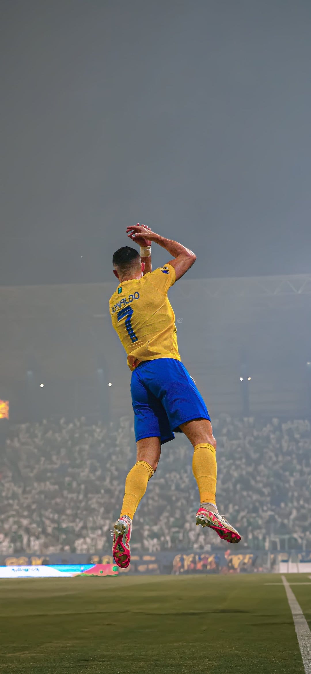 Cristiano Ronaldo leaps mid-air in a yellow jersey and blue shorts during a soccer match in a crowded stadium.