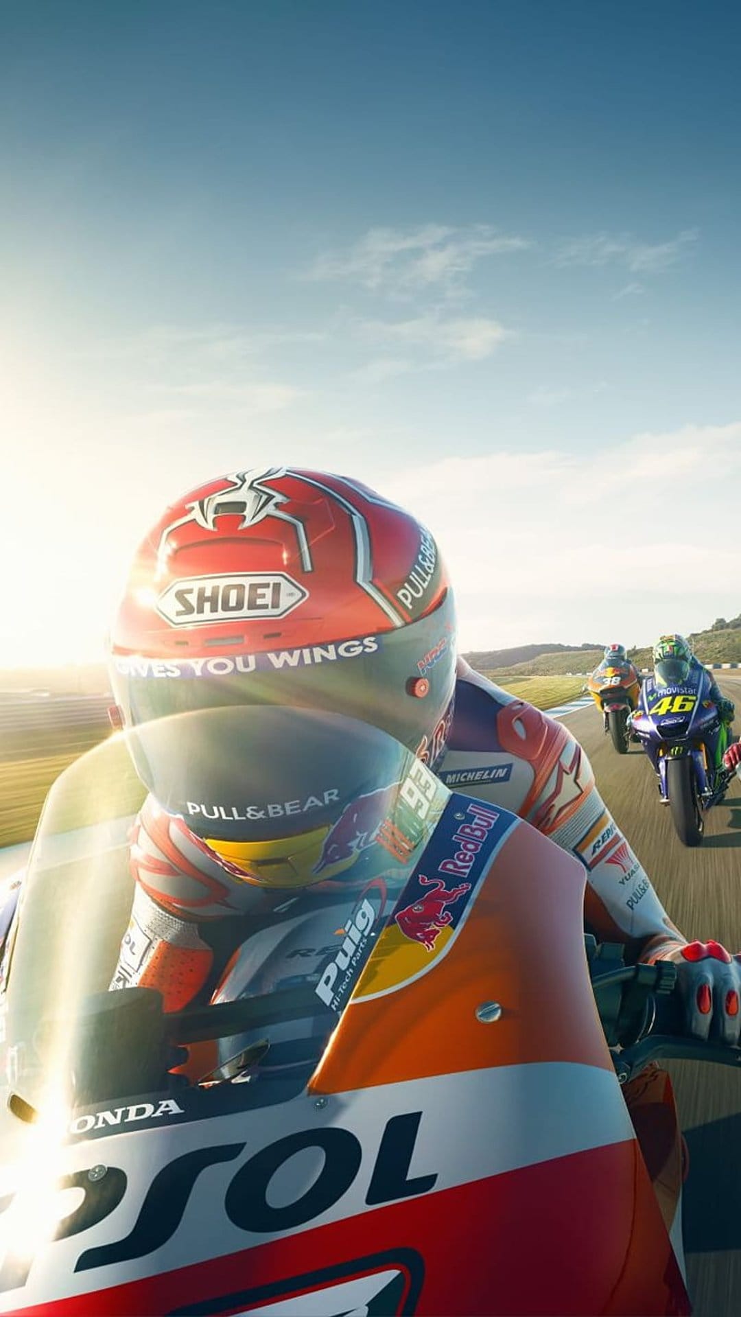 Motorcycle racer in a red helmet leans into a track corner with blue and yellow bikes blurred in the distance.