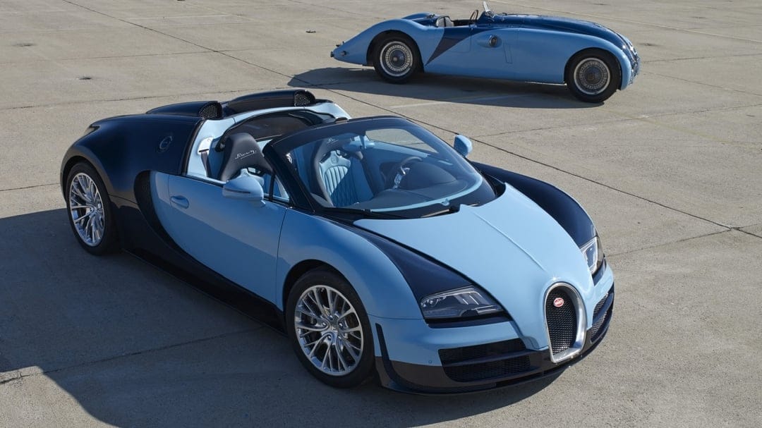 A modern blue Bugatti Veyron and a vintage racing car parked on a wide concrete airfield in bright sunlight.