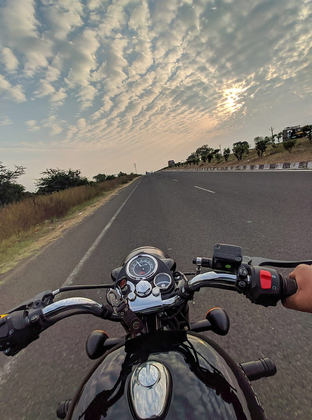 Motorcyclist POV riding a black bike on a desert highway under a dramatic sunset sky with rippling orange clouds.