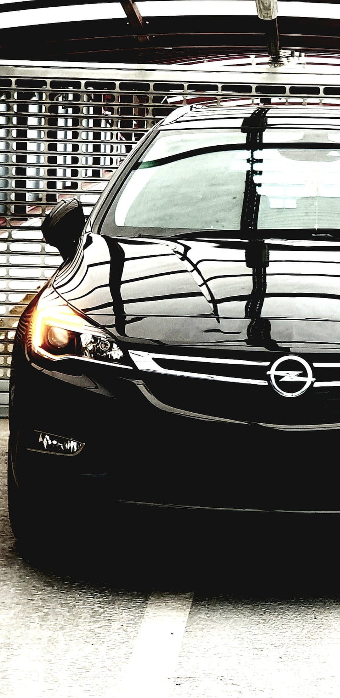 Black Opel Astra front grille with an illuminated orange headlight and chrome logo against a metal shutter.