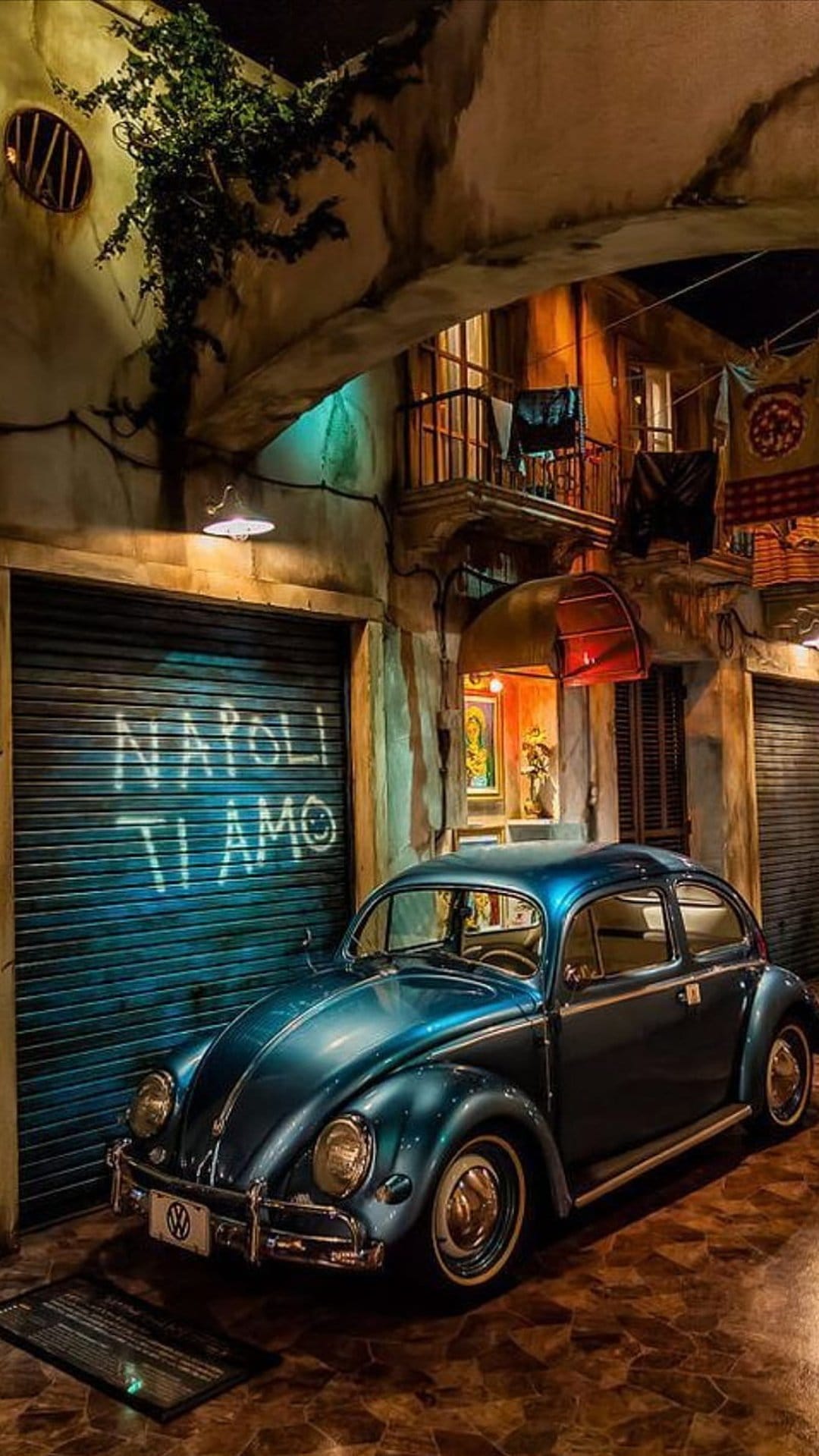 Blue Volkswagen Beetle parked in a narrow Italian street at night with Napoli Ti Amo spray-painted on a door.