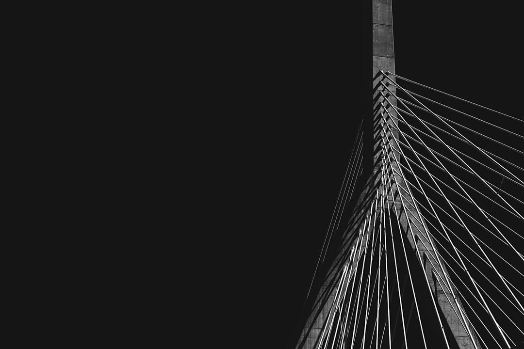 Modern bridge tower and symmetrical white cables set against a dark sky in high contrast black and white.