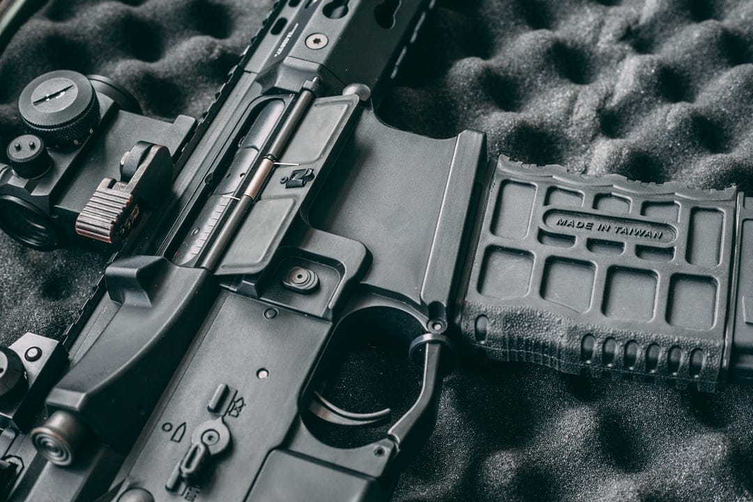 Black AR-15 rifle receiver and magazine with tactical sight on textured dark foam padding in a storage case.