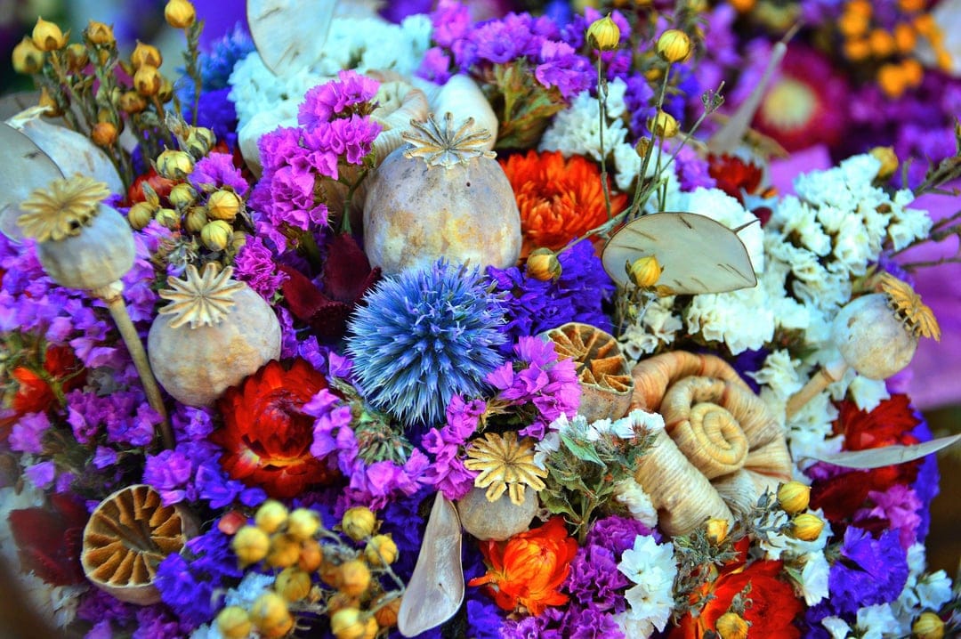 Dried poppy pods, blue thistle, and orange citrus slices arranged in a dense, textured rustic floral bouquet.