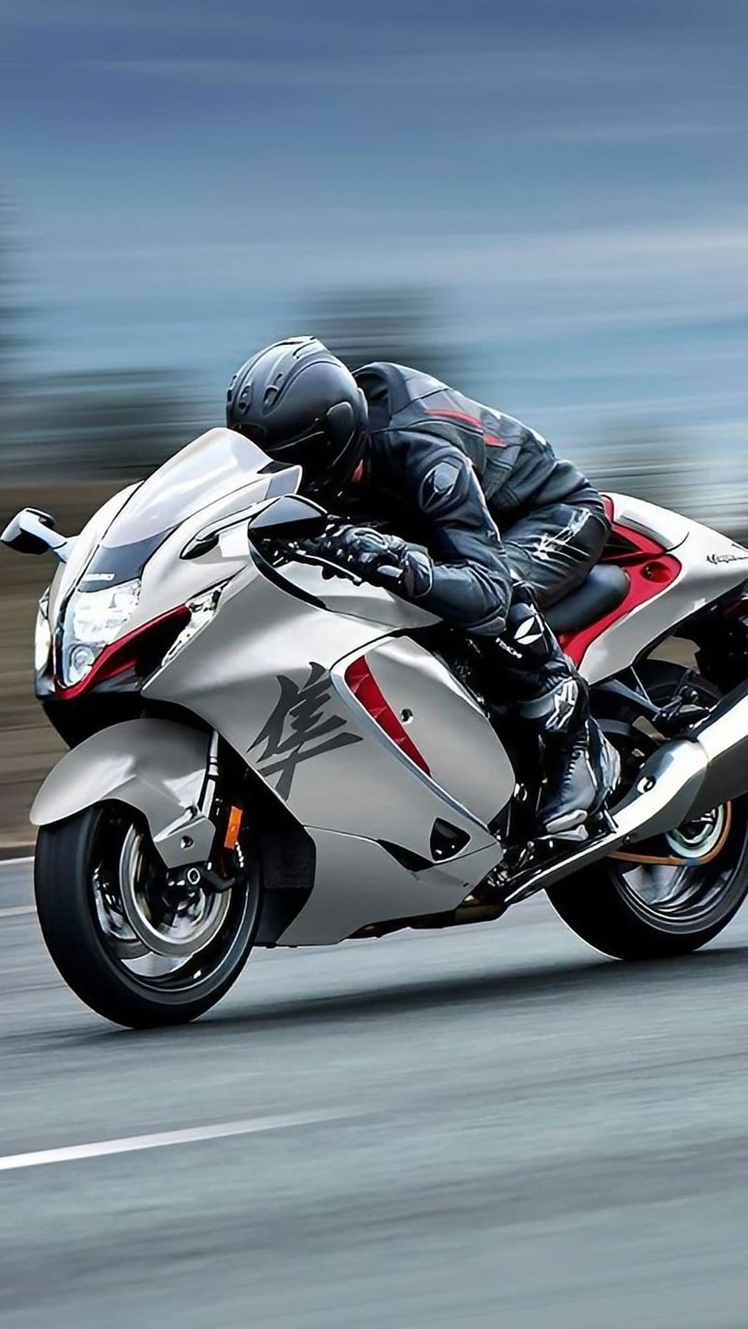 Suzuki Hayabusa rider in silver gear leans into a turn on a blurred asphalt road with vibrant red bike accents.