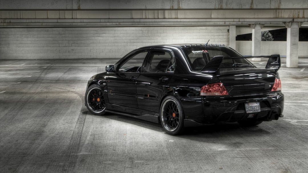 Rear view of a black Mitsubishi Lancer Evolution with a large spoiler in a gray concrete parking garage.