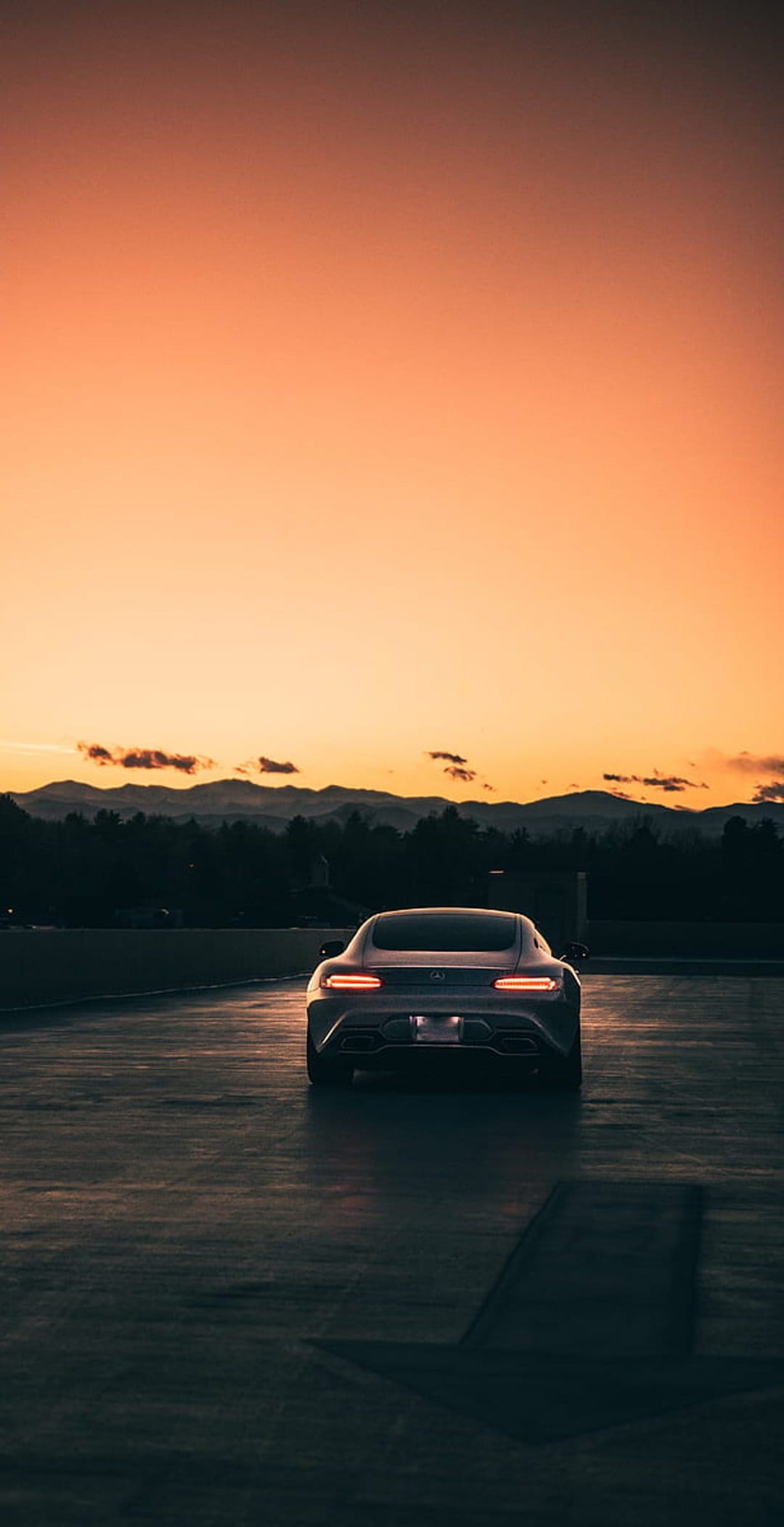 Mercedes-AMG GT sports car rear view on asphalt with orange sunset skies and silhouetted mountain peaks.