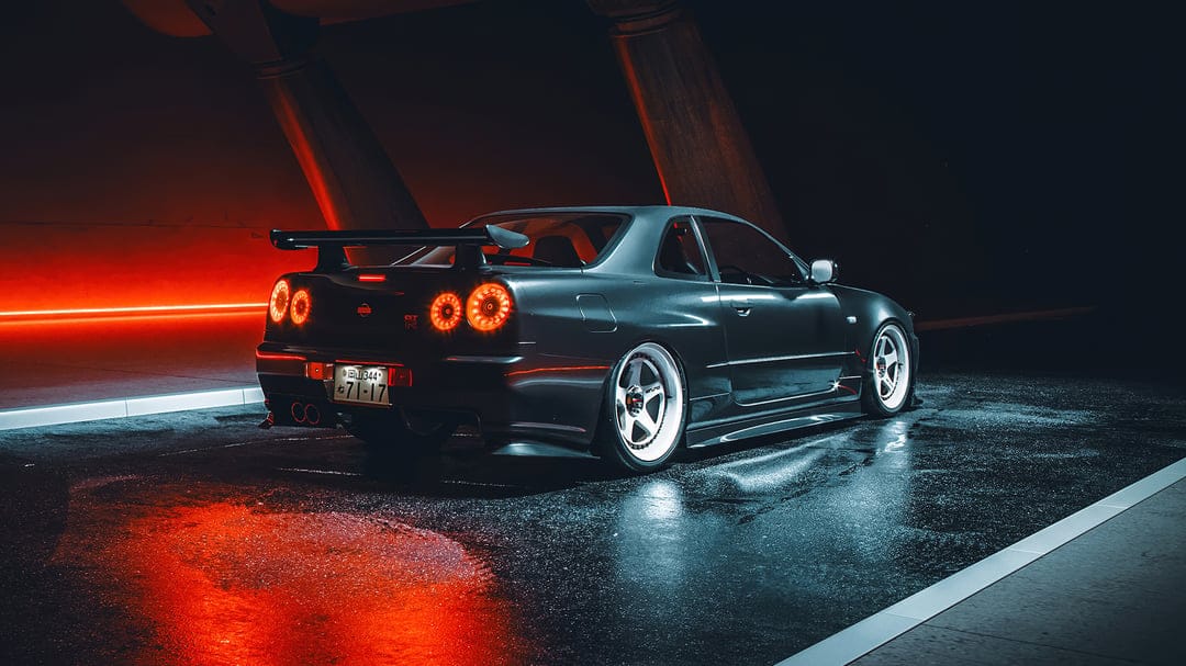 Nissan Skyline GT-R R34 with glowing red taillights parked on wet asphalt under cinematic neon lights.