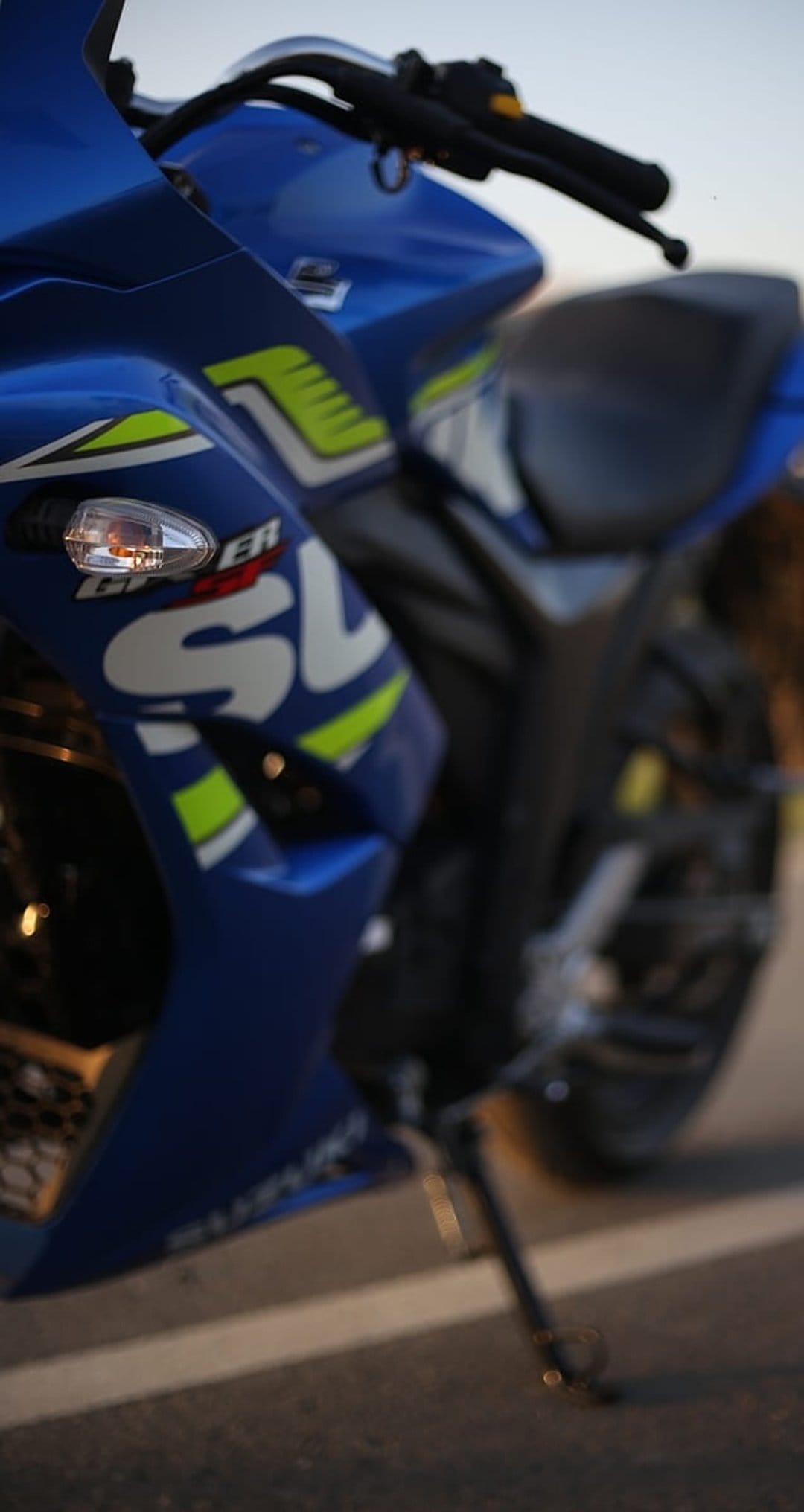 Blue Suzuki GSX-R sport motorcycle with lime green accents parked on a paved road with white line markings.