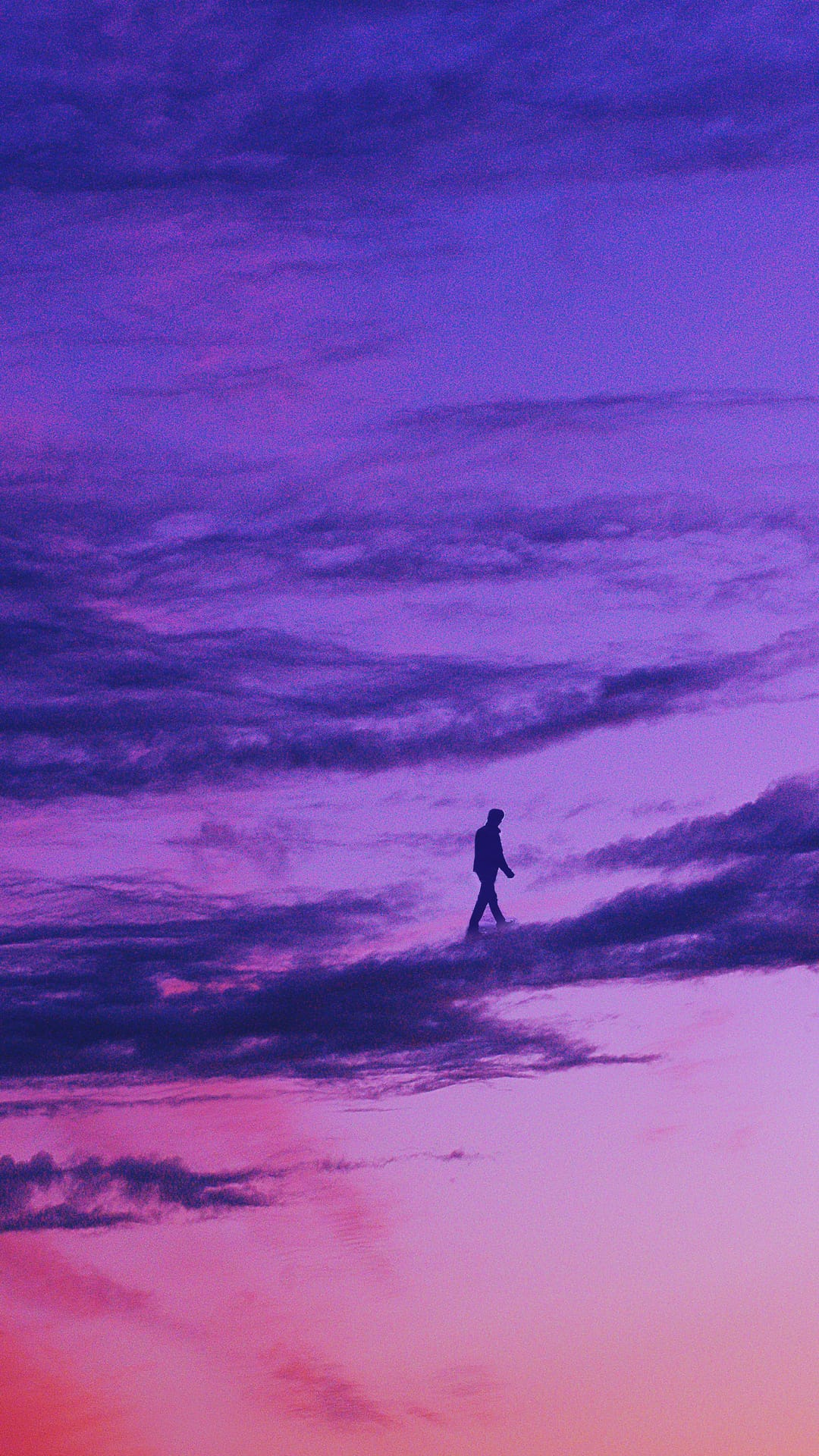 Person silhouette walking on dark clouds against a vibrant purple and pink sky in a vertical perspective.