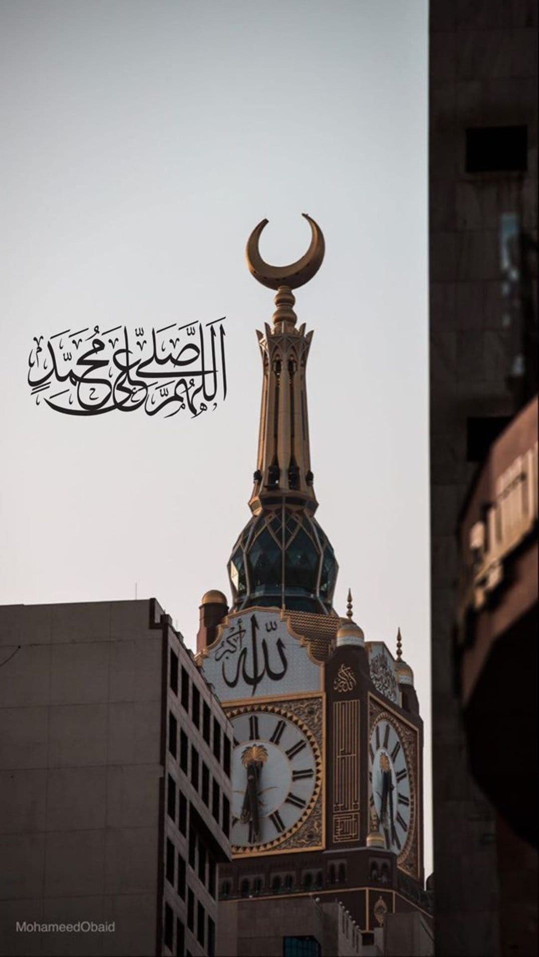 Makkah Clock Tower with gold Arabic calligraphy, large clock faces, and a crescent moon finial under a blue sky.