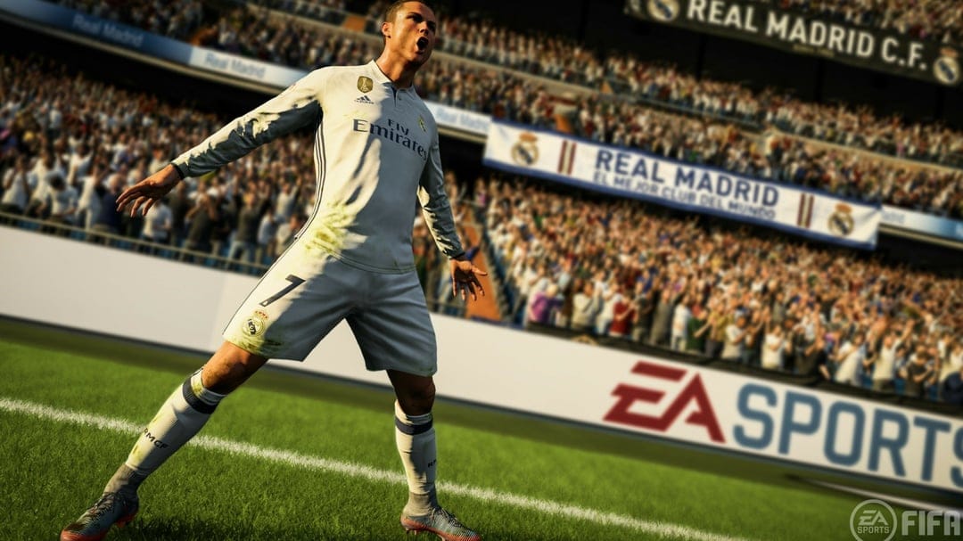 Cristiano Ronaldo celebrates in a white Real Madrid kit on a green pitch with a blurred stadium crowd behind.