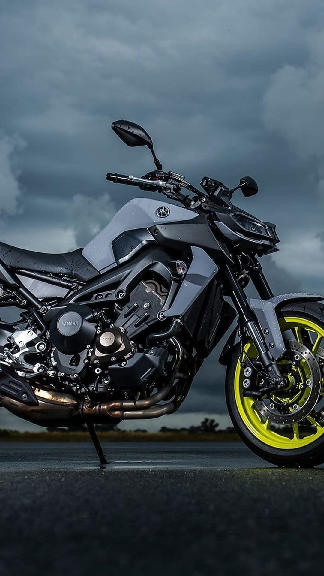 Yamaha MT-09 motorcycle with neon yellow rims parked on asphalt under a dark, cloudy sky in portrait orientation.