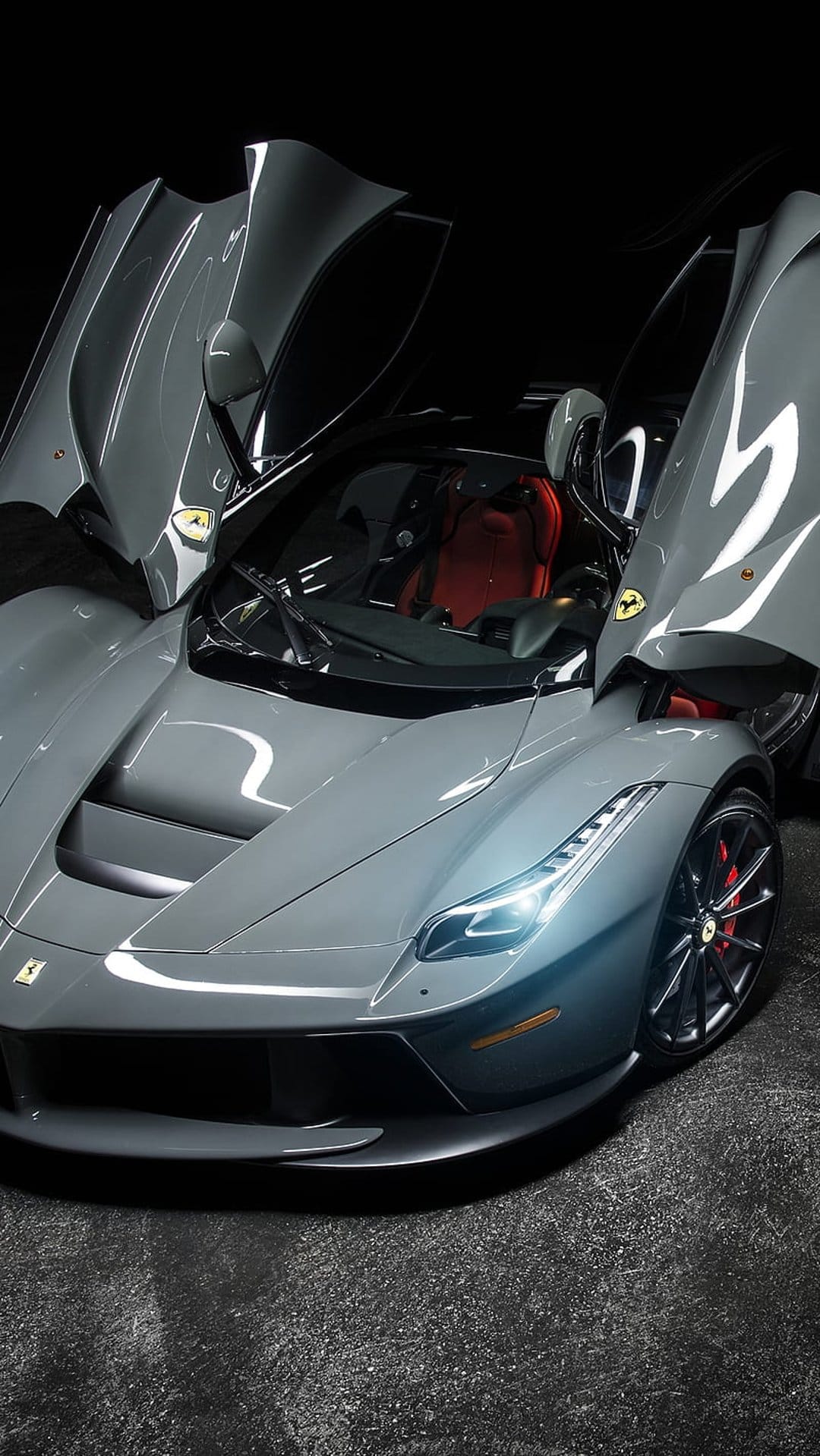Grey Ferrari LaFerrari with open dihedral doors reveals a red leather interior against a dark studio background.