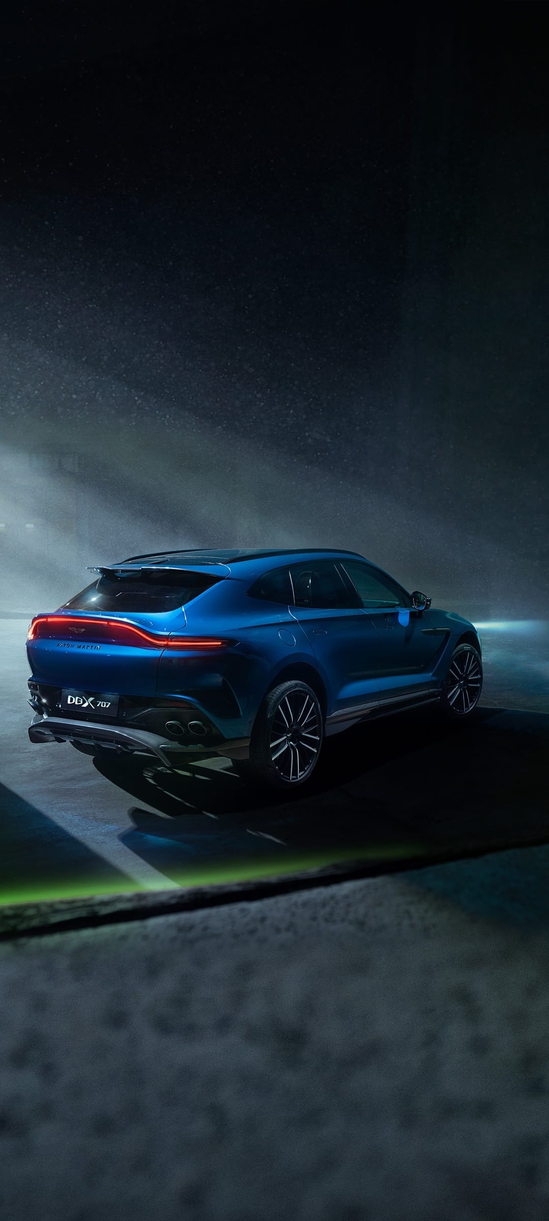 Blue Aston Martin DBX 707 SUV with glowing red taillights parked in a dark misty environment under cinematic light.