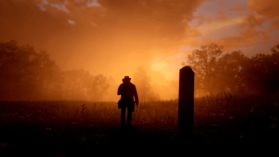 Silhouette of a cowboy walking away through a foggy orange meadow at sunset beside a grave marker.
